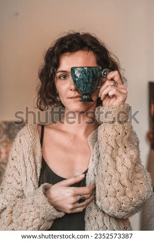 Portrait of young Caucasian woman covering half her face with a handmade clay mug.Small business,entrepreneurship,creative work,hobby,leisure concept. 