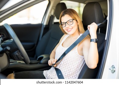 Portrait Of Young Caucasian Woman With Glasses Sitting In Driving Seat Of Car, Fastening Safety Belt And Making En Eye Contact