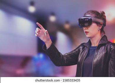 Portrait of young Caucasian woman using augmented and virtual reality with holographic hololens glasses. Pink, magenta and blue blurred background. Future technology concept.