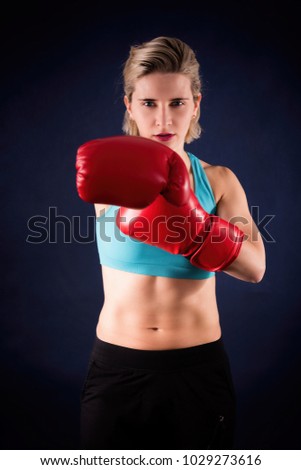 Similar – Close up front portrait of one young athletic woman in sportswear in gym over dark background, standing in boxing stance with hands and fists, looking at camera