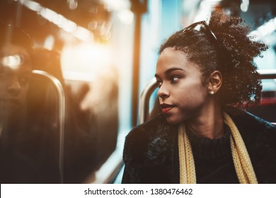 The portrait of a young charming African-American female pensively looking outside the carriage window while sitting indoors of a metro train; Brazilian girl in a subway train, shallow depth of field - Powered by Shutterstock