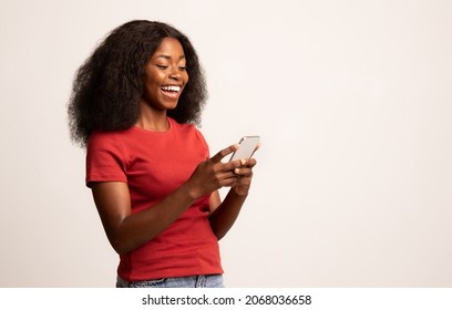 Portrait Of Young Cheerful Black Lady Using Smartphone For Messaging With Friends, Happy African American Lady Texting On Cellphone While Standing Over White Studio Background, Copy Space