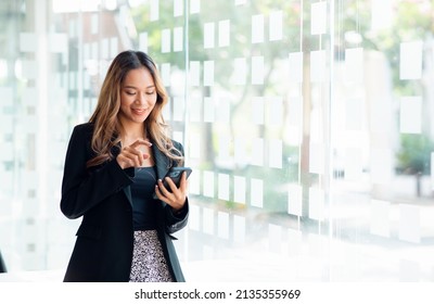 Portrait of a young cheerful excited bearded Asian woman using mobile phone standing on an office 