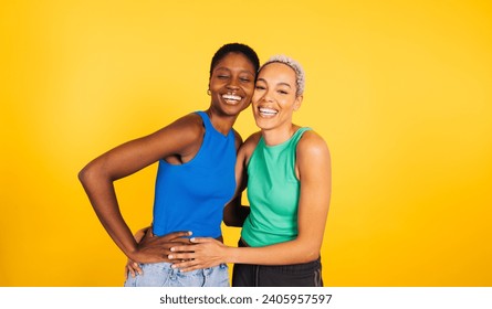 Portrait of a young cheerful female couple in front of a yellow background at studio.Two women together at studio. - Powered by Shutterstock