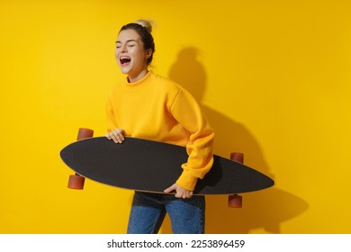 Portrait of young cheerful girl with longboard against yellow background - Shutterstock ID 2253896459