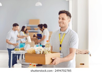 Portrait of a young cheerful male volunteer working at charity center giving free food donations in charitable foundation. Humanitarian aid, volunteering and social help for poor concept. - Powered by Shutterstock