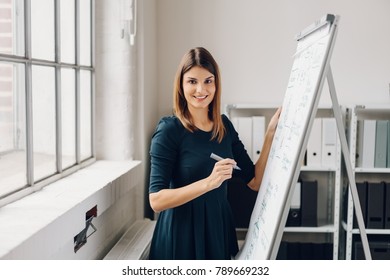 Portrait Of Young Cheerful Woman Holding Marker Pen Standing By Flip Chart