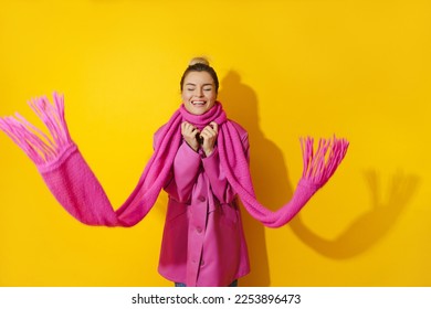 Portrait of young cheerful woman wearing pink coat and wool scarf against yellow background - Shutterstock ID 2253896473
