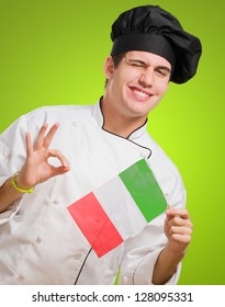 Portrait Of A Young Chef Holding Italian Flag And Winking against a green background
