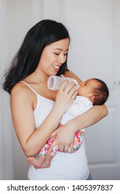 Portrait Of Young Chinese Asian Mother Feeding Newborn Baby Son Daughter With Milk Formula From Bottle. Authentic Lifestyle Candid Real Moment. Real Motherhood Family Life Concept.