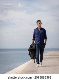 Portrait of a young classy entrepreneur relaxing alone along the Lisbon riverside in Portugal. Classy business man wearing a blue elegant shirt and formal outfit. Successful lifestyle concept.