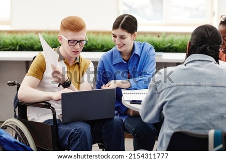 Portrait of young college student in wheelchair using laptop while participating in group discussion with friends, copy space