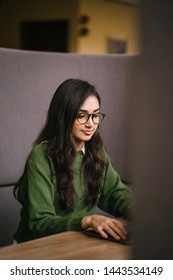 Portrait Of A Young, Confident And Attractive Indian Asian Student Working Or Studying On Her Laptop As She Sits In A Booth. She Is Dressed In A Preppy Sweater And Shirt And Glasses. 