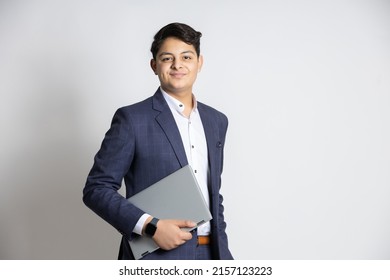 Portrait of young confident Indian teenager boy wearing suit holding laptop in hand looking at camera isolated on white studio background. - Shutterstock ID 2157123223