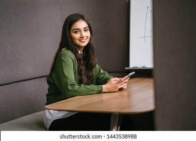 Portrait Of A Young, Confident, Intelligent-looking And Attractive Indian Asian Woman Using Her Smartphone. She Is Wearing A Preppy Green Sweater And Smiling Happily. 