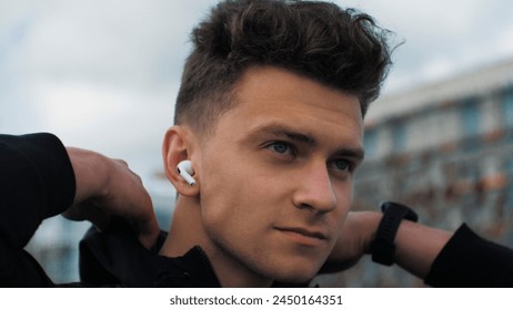 Portrait of a young confident man. He adjusts his jacket and prepares to run. Listens to music in headphones. In the city park - Powered by Shutterstock