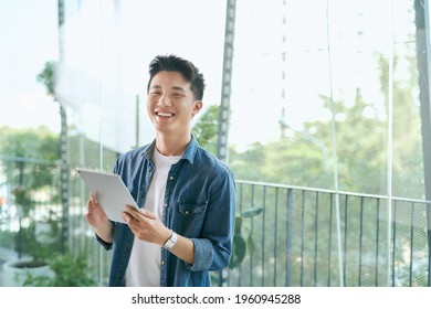 Portrait of a young confident smiling indian man holding a tablet and looking into the distance - Powered by Shutterstock