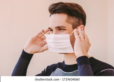 Portrait Of Young Confident Sports Man Listening Music In Wireless Earbuds And Putting On Medical Face Mask. Happy Sports Man Wearing Protective Mask And Smiling. COVID-19 Home Quarantine Training