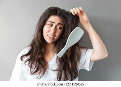 Portrait of young confused woman holds a tangled strand of her hair with a comb stuck in it. The concept of trichology and hair care.