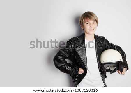 Portrait of Young cool beautiful teen kid in black leather jacket and holding hand white moto helmet smiling on white background