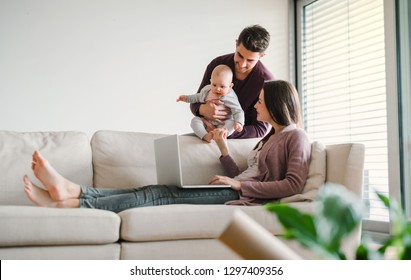 A portrait of young couple with a baby at home, using laptop. - Powered by Shutterstock