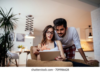 Portrait of a young couple enjoying using digital tablet indoors.