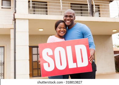 Portrait Of Young Couple Holding Sold Sign Outside Their House