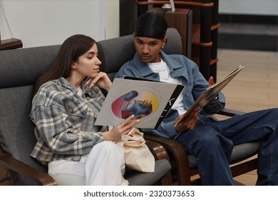 Portrait of young couple listening to vinyl records in music store and lounging in chairs - Powered by Shutterstock