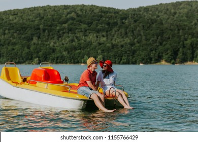 Portrait of young couple in love talking while pedal boating on the lake. Cheerful man and woman relaxing on pedal boat on hot sunny day.