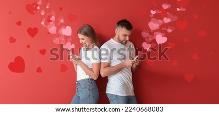 Portrait of young couple with mobile phones chatting online on red background. Valentine's Day celebration