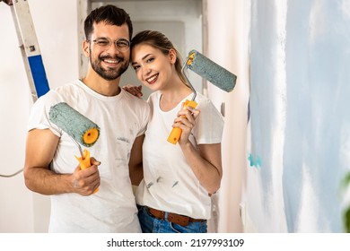 Portrait Of Young Couple Painting Wall In Their Home.