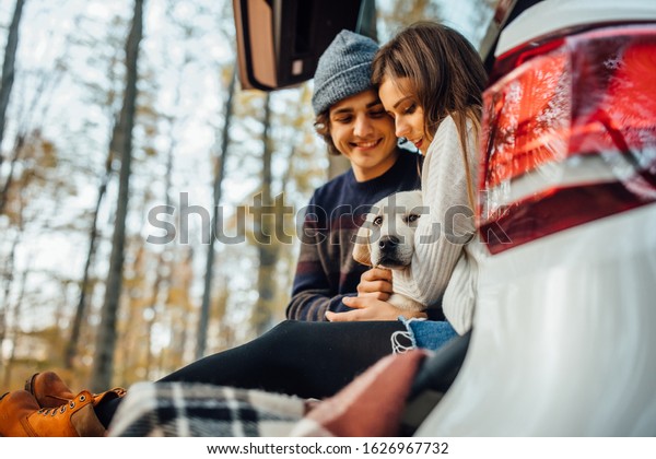 Portrait of young couple resting with dog in autumn\
park sitting in the\
car.