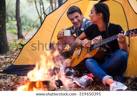 Portrait of a young couple sitting with guitar near bonfire in the forest