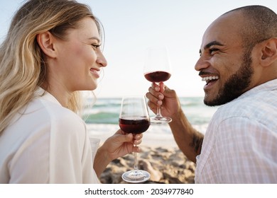 Portrait Of A Young Couple Sitting On The Beach And Drinking Wine