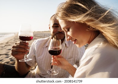 Portrait Of A Young Couple Sitting On The Beach And Drinking Wine