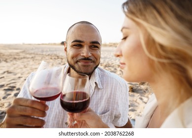 Portrait Of A Young Couple Sitting On The Beach And Drinking Wine