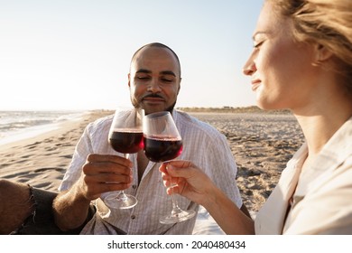 Portrait Of A Young Couple Sitting On The Beach And Drinking Wine