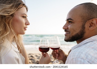 Portrait Of A Young Couple Sitting On The Beach And Drinking Wine