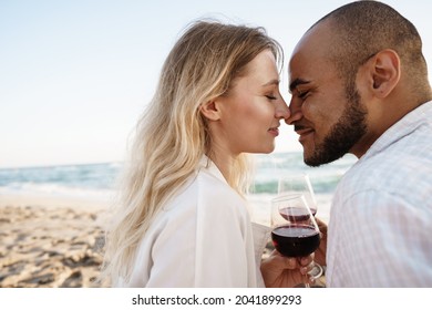 Portrait Of A Young Couple Sitting On The Beach And Drinking Wine