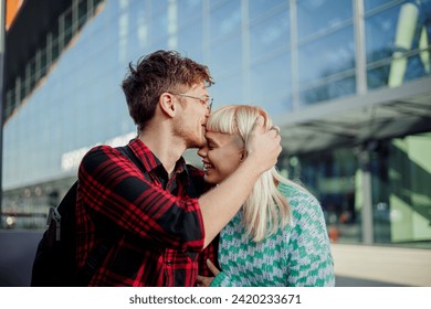 Portrait of a young couple sitting on a city street downtown and kissing. A trendy man is kissing his girlfriend in forehead while hugging her. An affectionate couple is having romantic moments. - Powered by Shutterstock