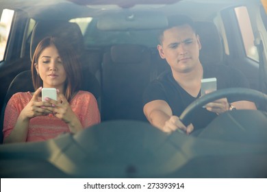 Portrait Of A Young Couple Texting And Driving Together, As Seen Through The Windshield