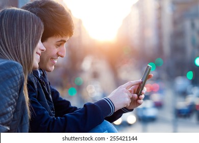 Portrait of young couple of tourist in town using mobile phone. 