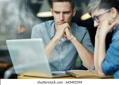 Portrait Of Young Creative Man And Woman Looking At Laptop Screen, Thinking, While Working In Cafe, Shot From Behind Glass Window