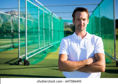 Portrait of young cricketer standing with arms crossed against net on field - Powered by Shutterstock