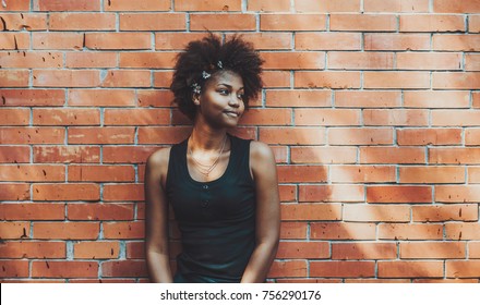 Portrait of young curly charming black female standing in front of brick wall of summer house; sweet cute teenage African American girl next to brick surface with daisies in her curly Afro hair - Powered by Shutterstock