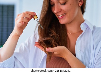 Portrait Of Young Cute Smiling Beautiful Caucasian Brunette Woman Using Dropper For Pampering And Moisturizing Hair Ends With Vitamin Essential Oil Serum