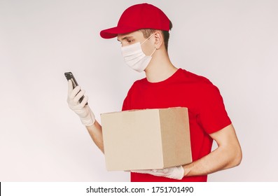 Portrait Young Delivery Guy In Uniform, Medical Face Mask, Protective Glove Use Mobile Phone, Hold Parcel Box In Hand Isolated On Background. Man Delivery Service Worker Carry Shipment And Smart Phone