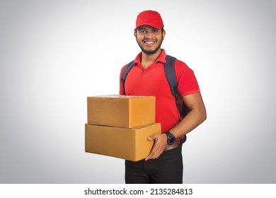 Portrait Of Young Delivery Man Holding Cardboard Box Against Grey Background