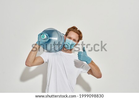 portrait of a young deliveryman with bottle of water on the shoulder and showing that everything is fine, isolated over the bright white background , wearing mask