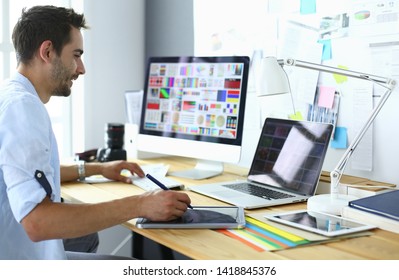 Porträt von jungen Designern, die im Grafikstudio vor Laptop und Computer sitzen, während sie online arbeiten.